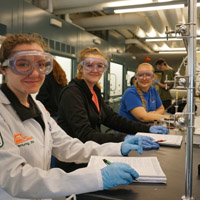 three students smile in a science lab with equipment